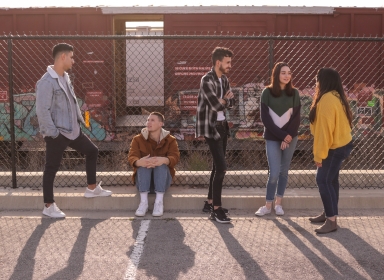 Billede af fem teenagers stående ved et hegn foran tog. Credit Eliott Reyna axtm0ee3yp4 Unsplash